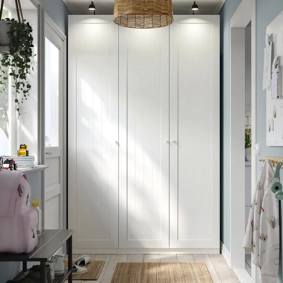 White PAX wardrobe with backpacks, toys, and bins, highlighted by pendant light.