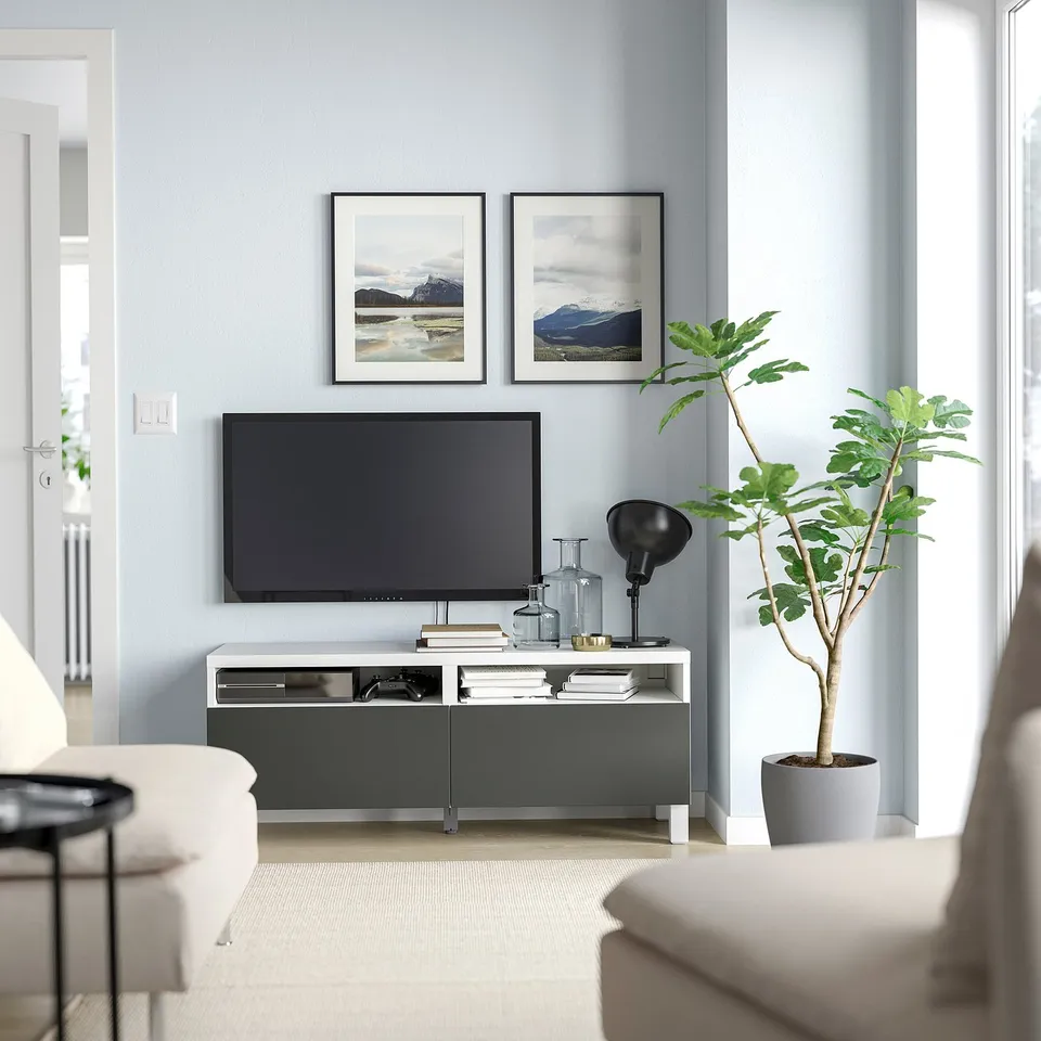 Modern living room with blue walls, BESTÅ tv stand, tv, mountain photos, white sofa, large plant.