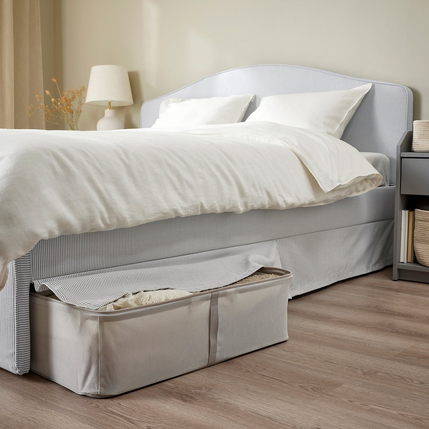 Neutral-toned bed with striped cover and plush headboard, featuring under-bed storage and a clean, cosy look.