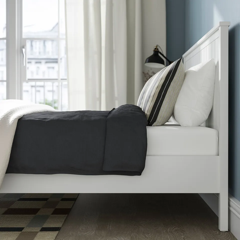 White bed with black blanket and striped pillows near window.