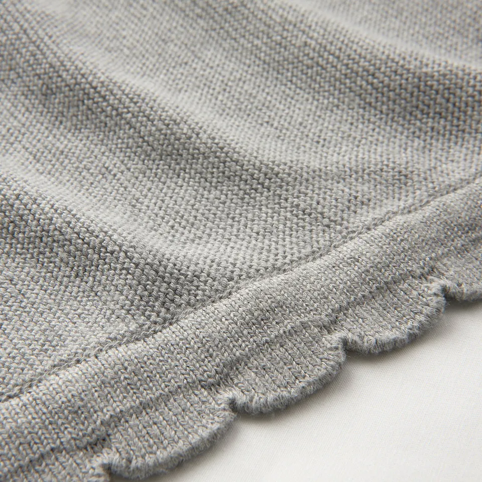 Close-up of soft, knitted blanket with scalloped edge, showcasing its texture and quality.