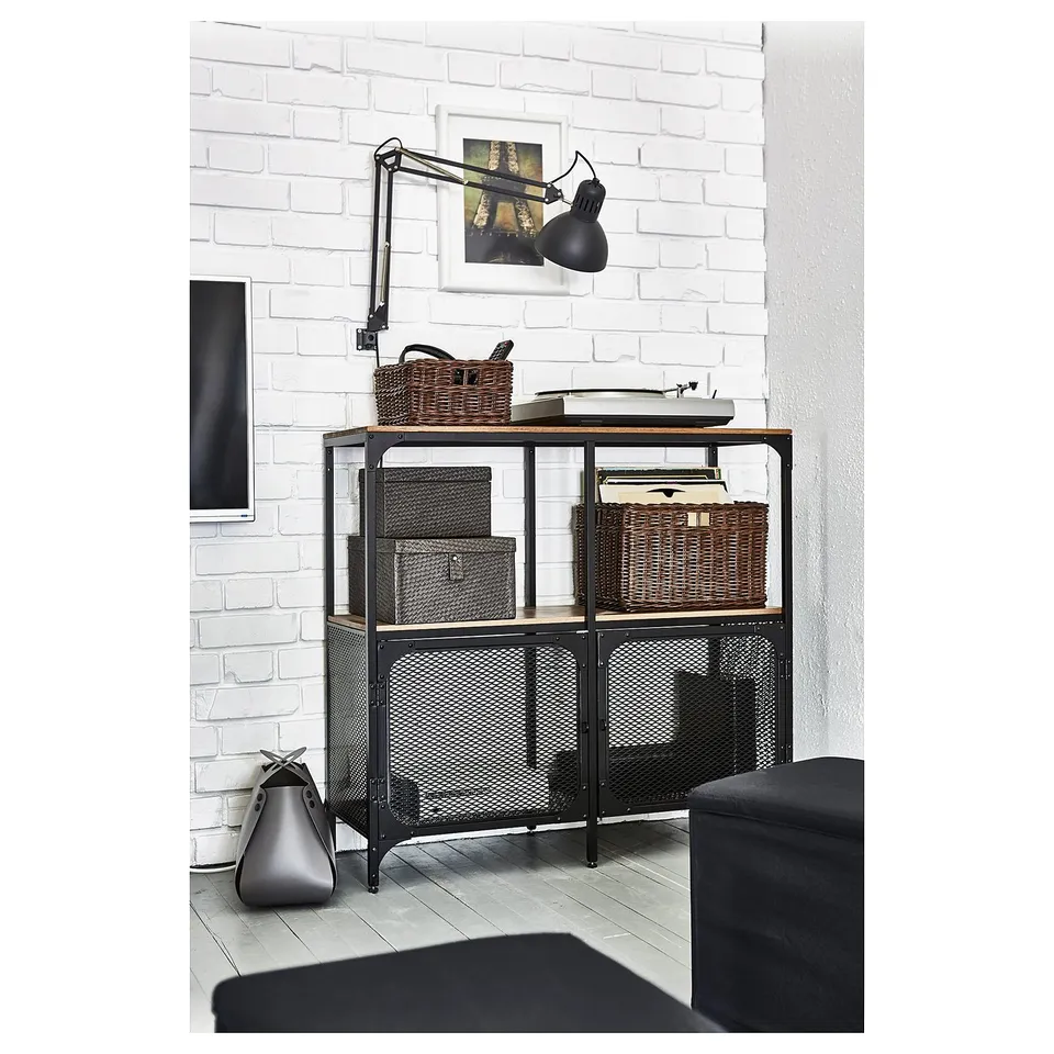 Industrial-style black metal and wood shelf with woven baskets, books, and lamp on brick wall.