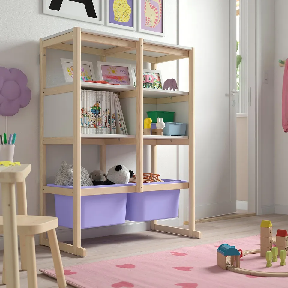Wooden FLISAT shelf with colourful toys and books, purple bins, near stools on pink rug.
