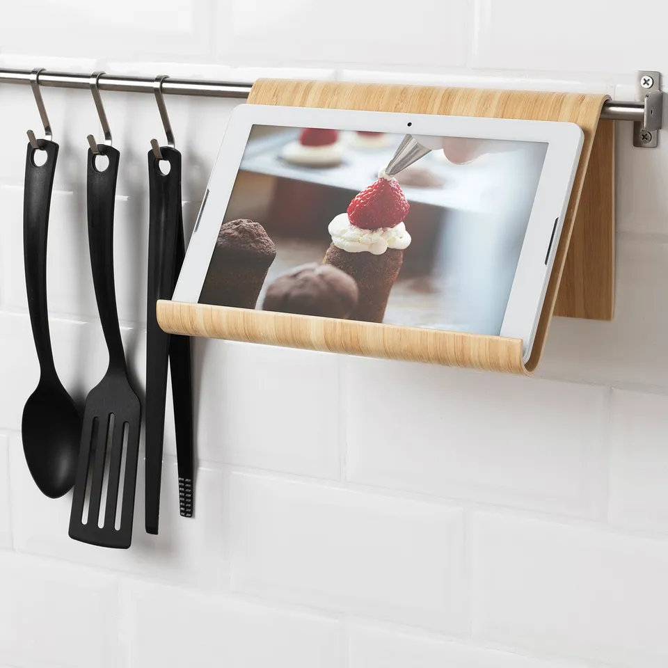 Tablet holder hangs on kitchen rail, displaying tablet with dessert recipe. Black utensils hang beside it.