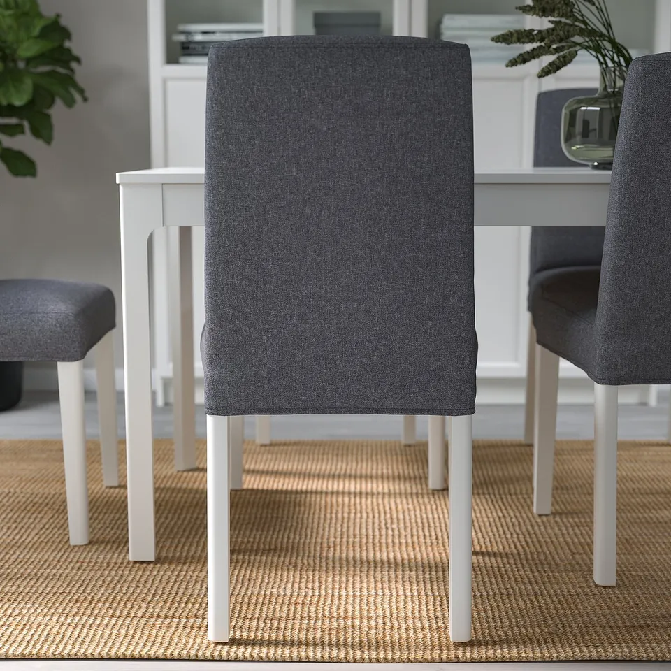 Three modern dining chairs in a kitchen. Grey upholstered seats with white wooden legs.