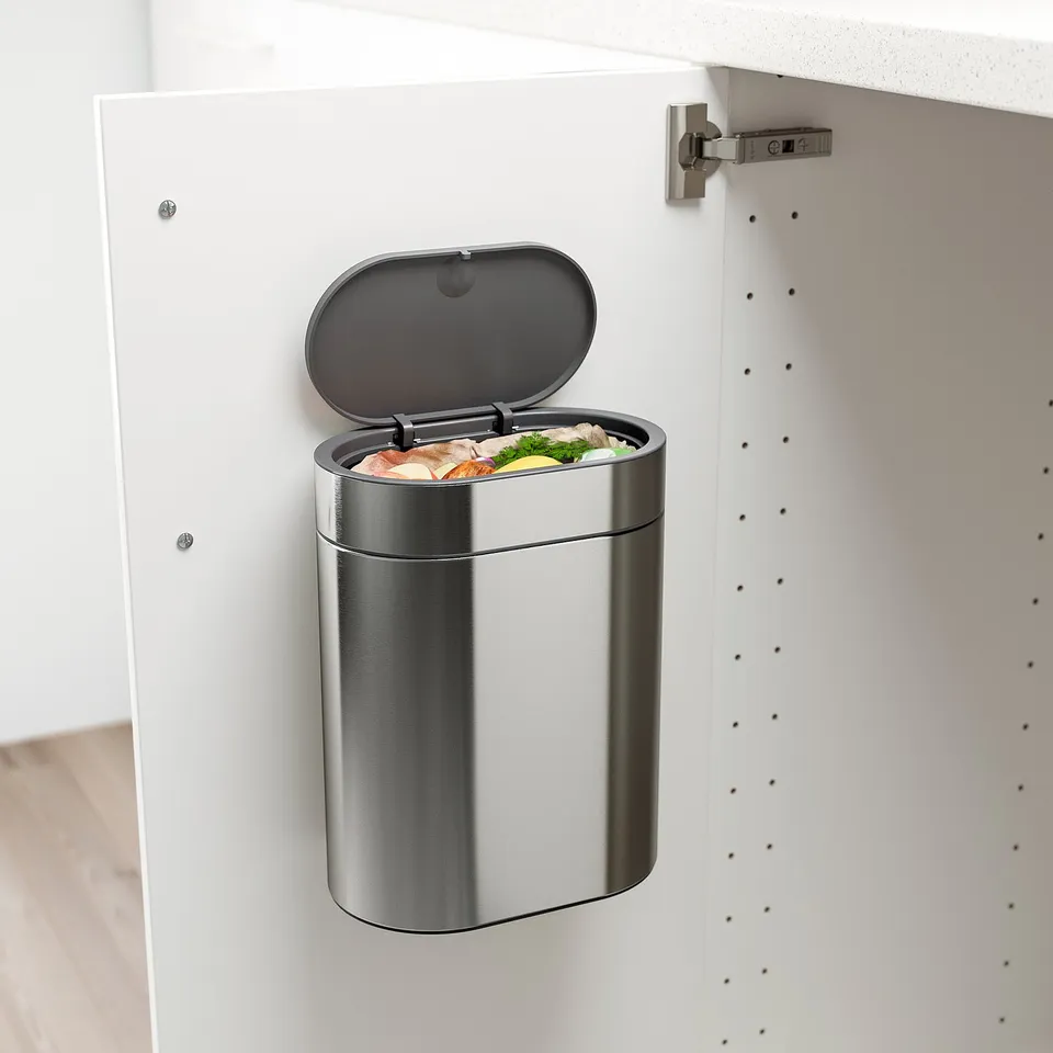 Stainless-steel under-cabinet rubbish with open lid showing food scraps.
