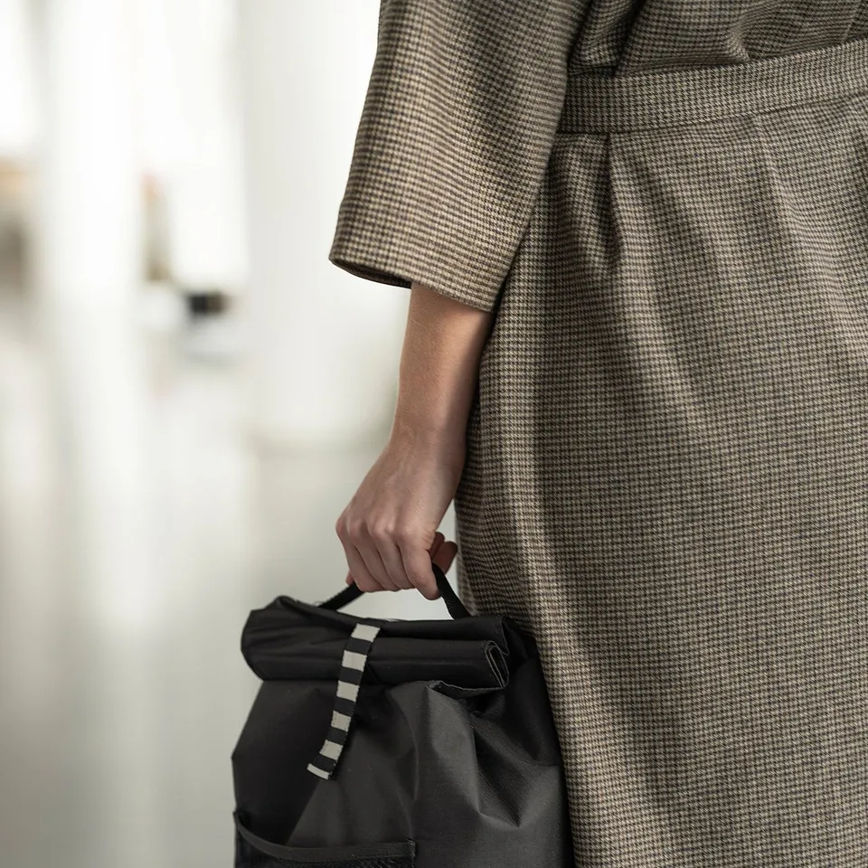 Person holding black, round-handled FRAMTUNG bag, chequered grey coat.