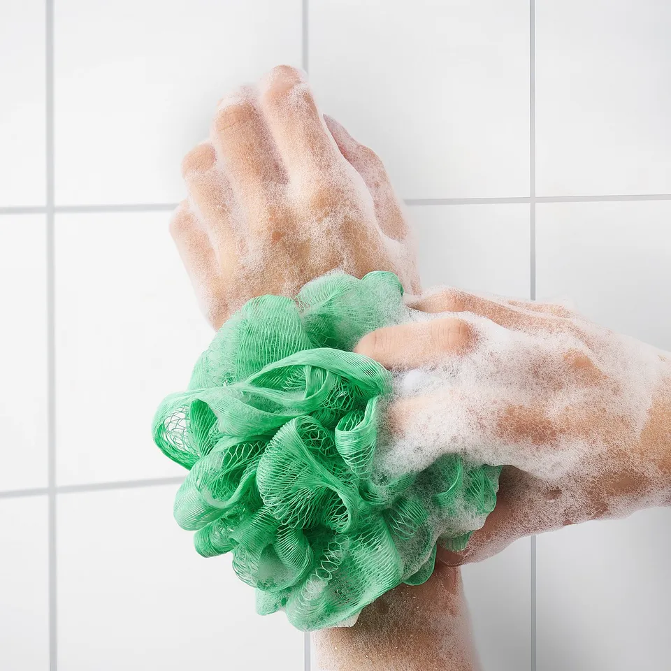 Person using green mesh body puff, creating soap suds for exfoliation.