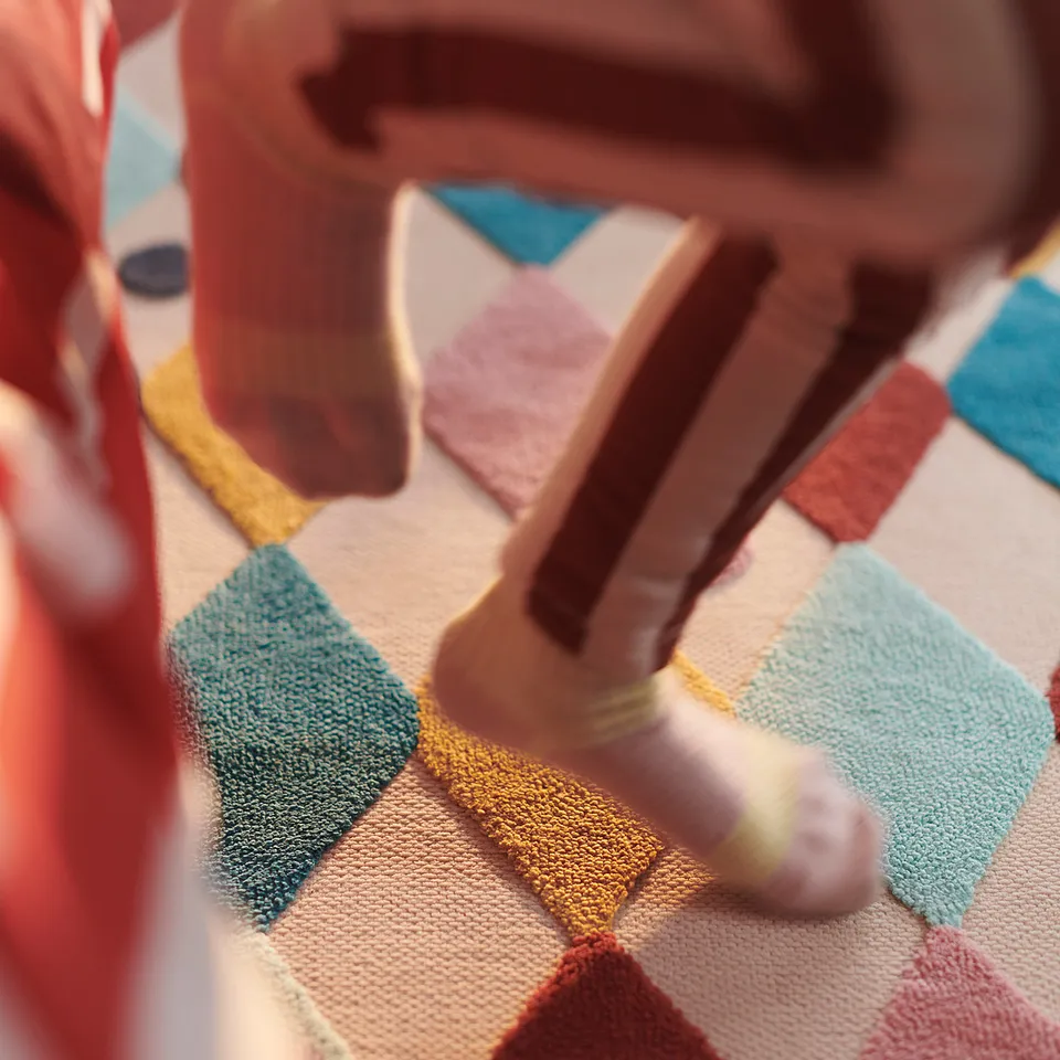 Children playing on colourful, soft harlequin rug. Bright diamond shapes, wooden toys, vibrant play area.