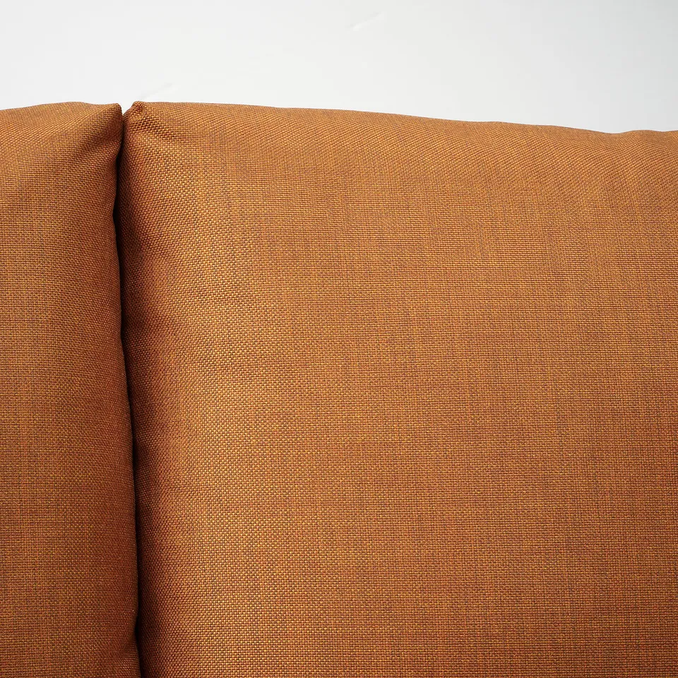 Close-up of an orange-brown fabric sofa, showing its smooth texture and stitched seams.