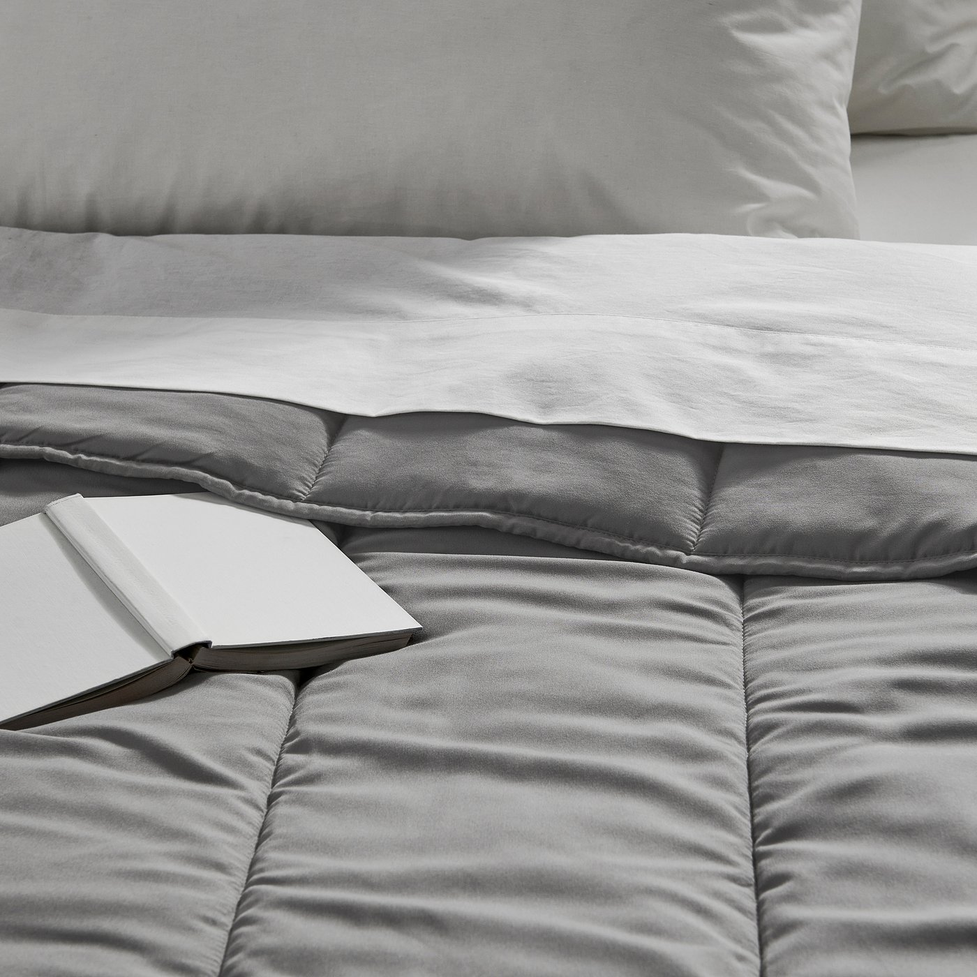 Grey comforter with silky smooth texture on bed, open book resting on it.