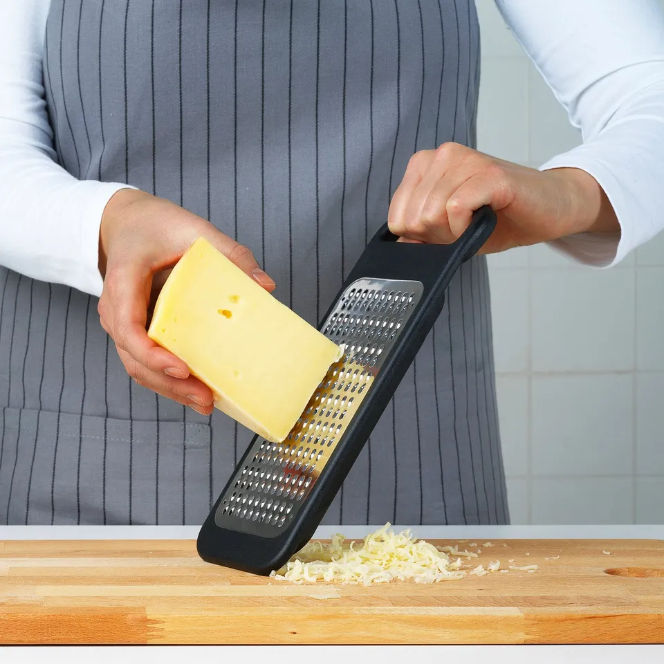 Person grates cheese with black ikea grater on wood.