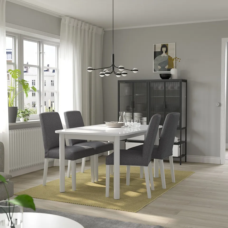 Modern dining with extendable table, grey chairs, yellow rug, pendant light, large window, black bookshelf.