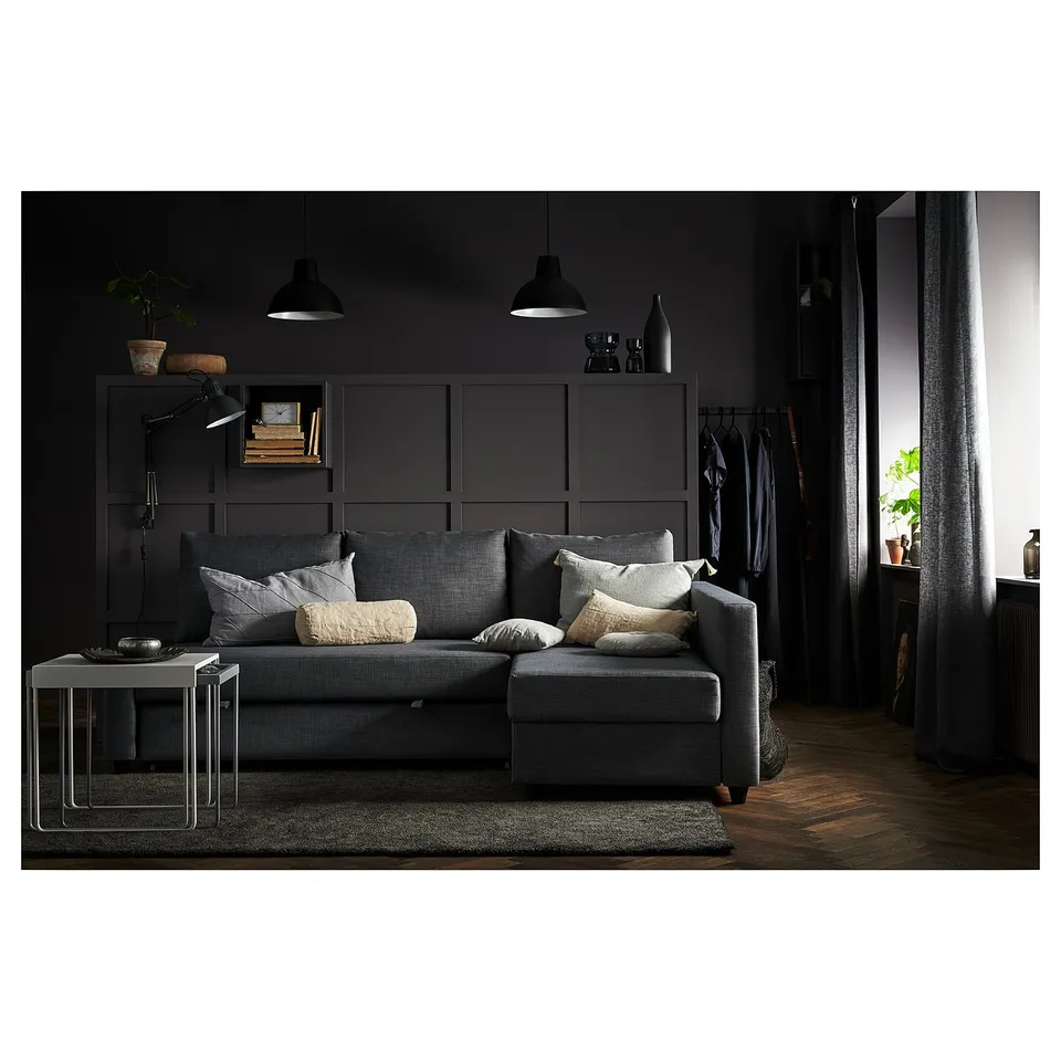 Modern dark grey convertible sofa with built-in storage, pillows, carpet, and hanging light fixtures.