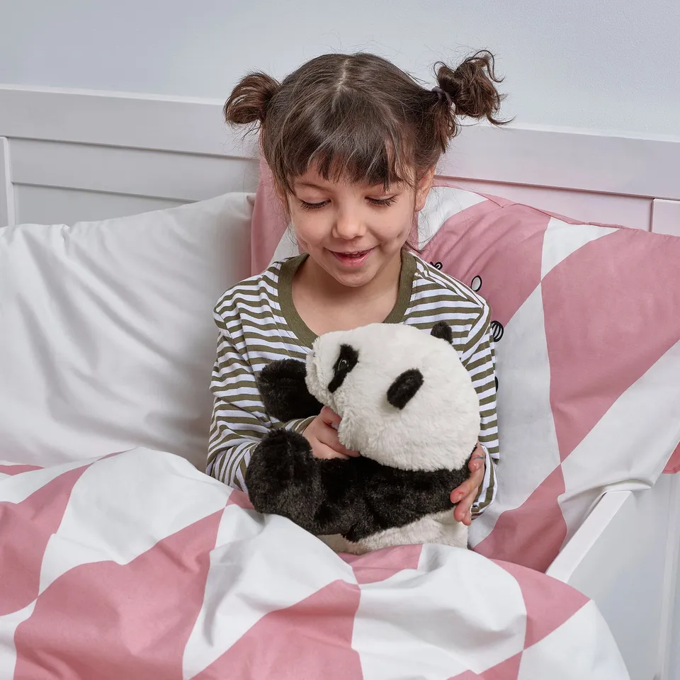 A young girl in striped pyjamas sits in bed, hugging a soft panda toy, symbolising comfort and companionship.