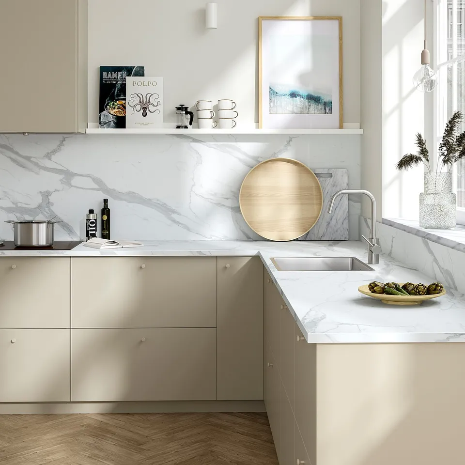 Modern kitchen with beige counter, marble backsplash, plants, and artichokes. Spacious with sink, light colours, dark floor.