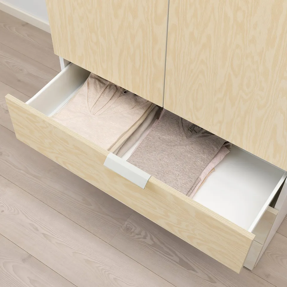 Wooden drawer open, revealing neatly folded clothes inside. Part of a storage system with light-colored frames.