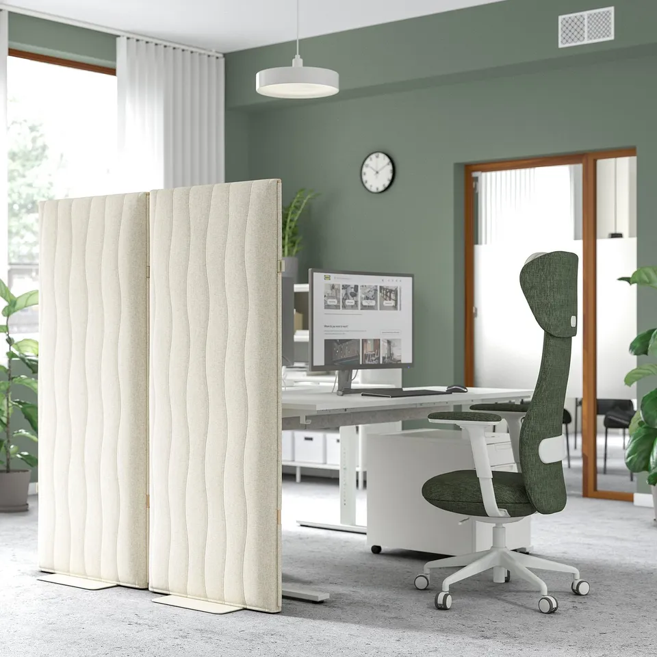 Beige office screen reduces noise, divides space. Tall, rippled, beside desk and chair.