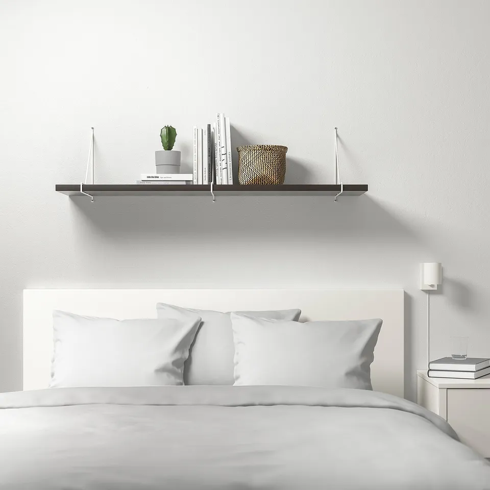 Minimalist bedroom with BERGSHULT shelf holding books, basket, cactus. White bed with pillows, bedside table beside.