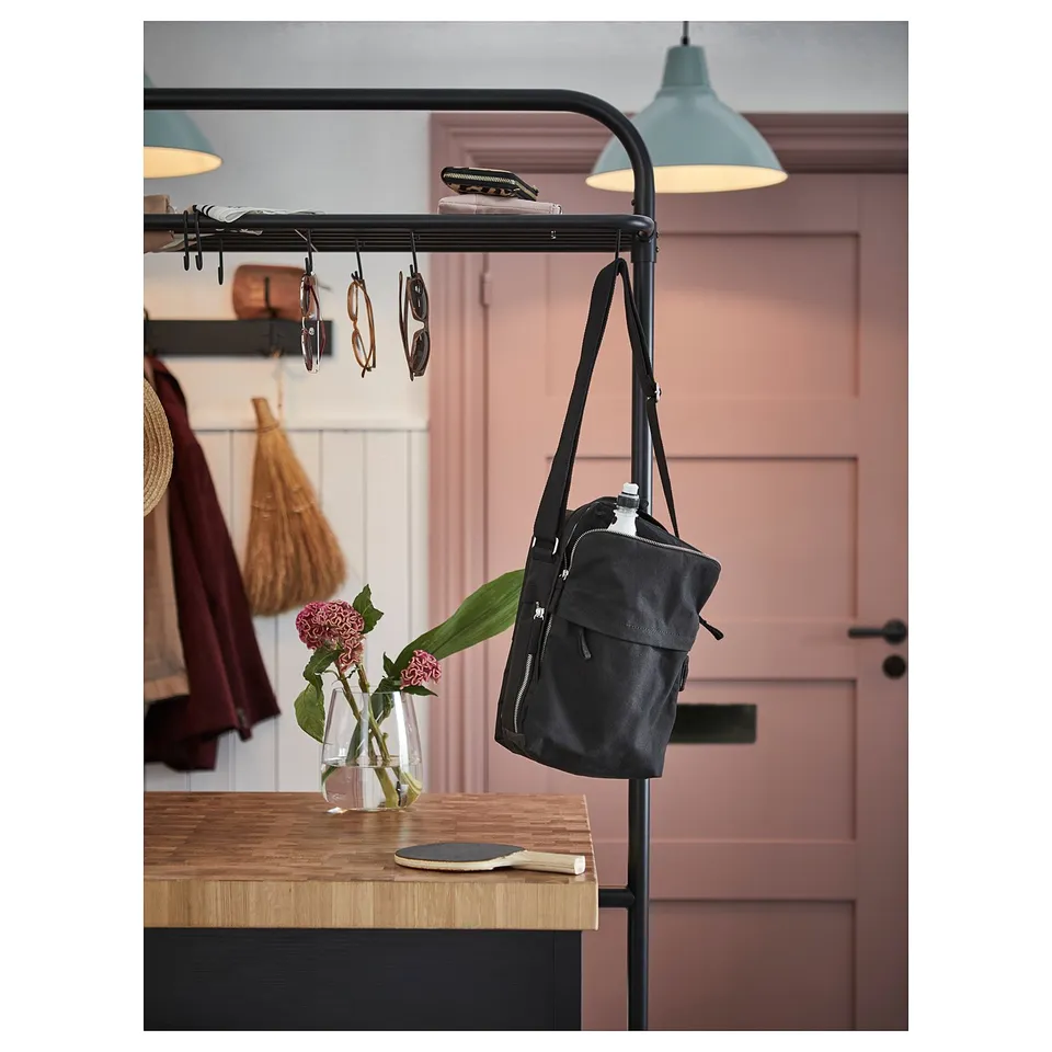 Black hanging bag on black metal rack near wooden table with vase of flowers.