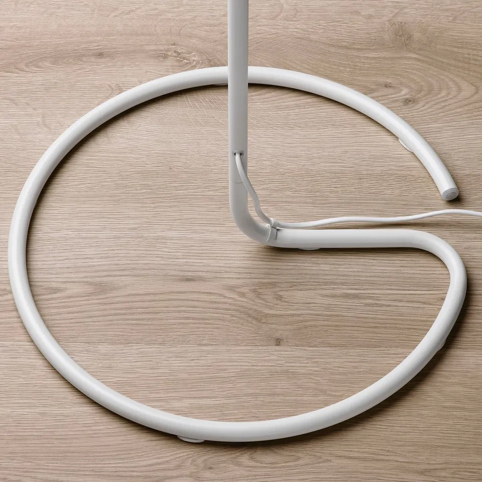 Modern floor lamp with sleek, white design and circular, soft shade resting on wooden floor.