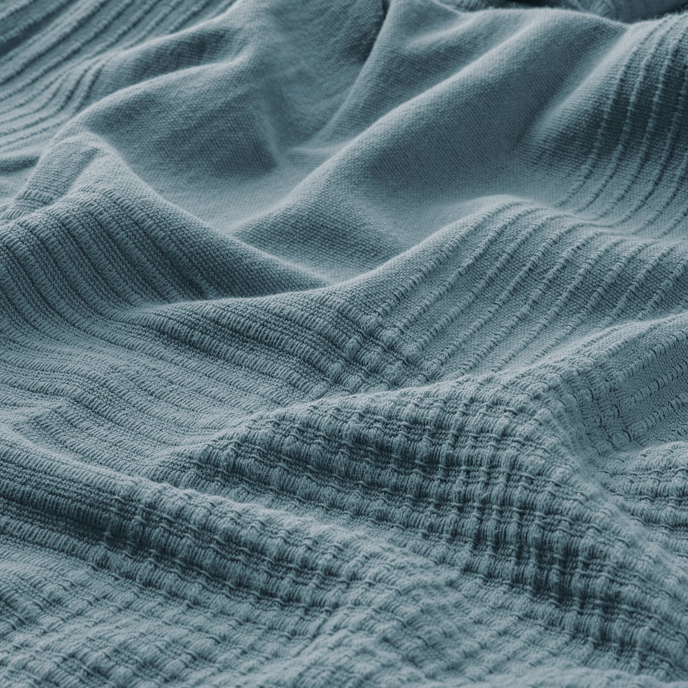 Close-up of soft, textured blue cotton bedspread, showcasing its weave and warmth.