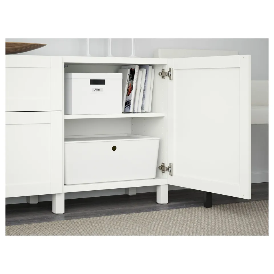 White BESTÅ storage unit, open door revealing storage box and magazines on adjustable shelf, soft closing hinges visible.