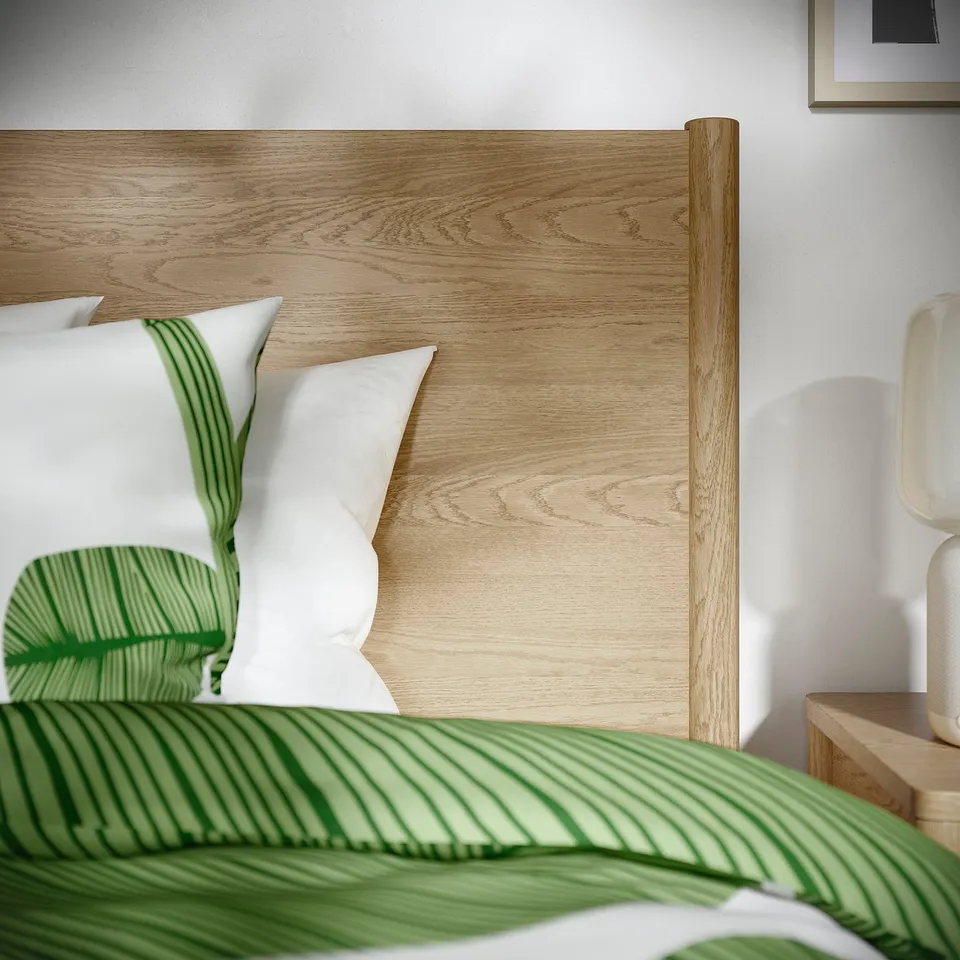 A modern bed with a wooden headboard featuring two white pillows and a green striped blanket, showcasing high-quality materials and design.