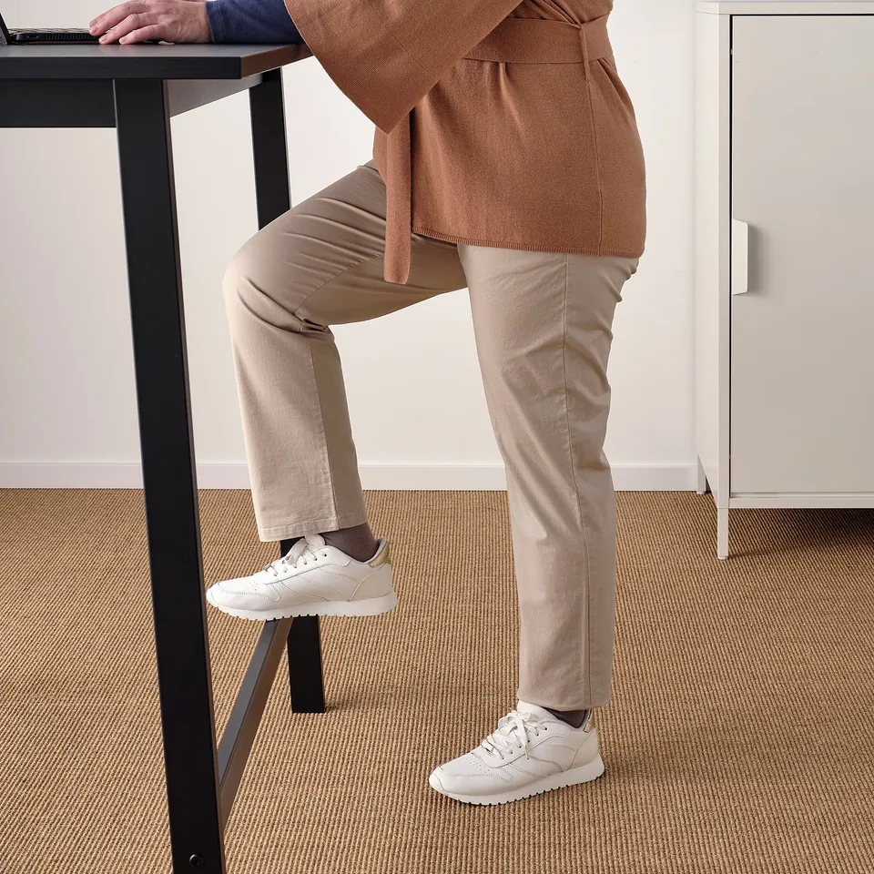 In a person is using a high table with a footrest, suitable for sitting or standing, ideal for meetings or long calls.