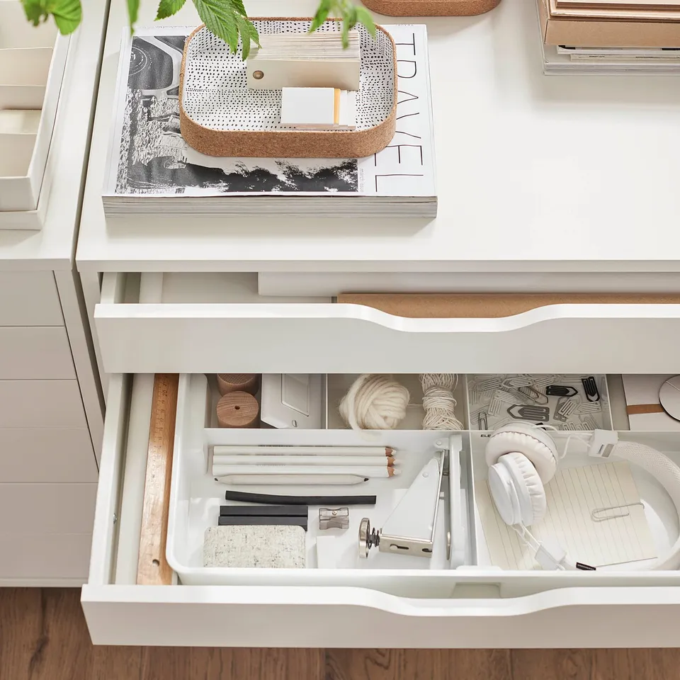 Organised desk drawer with KUGGIS white organiser holding art supplies, small tools, and headphones.