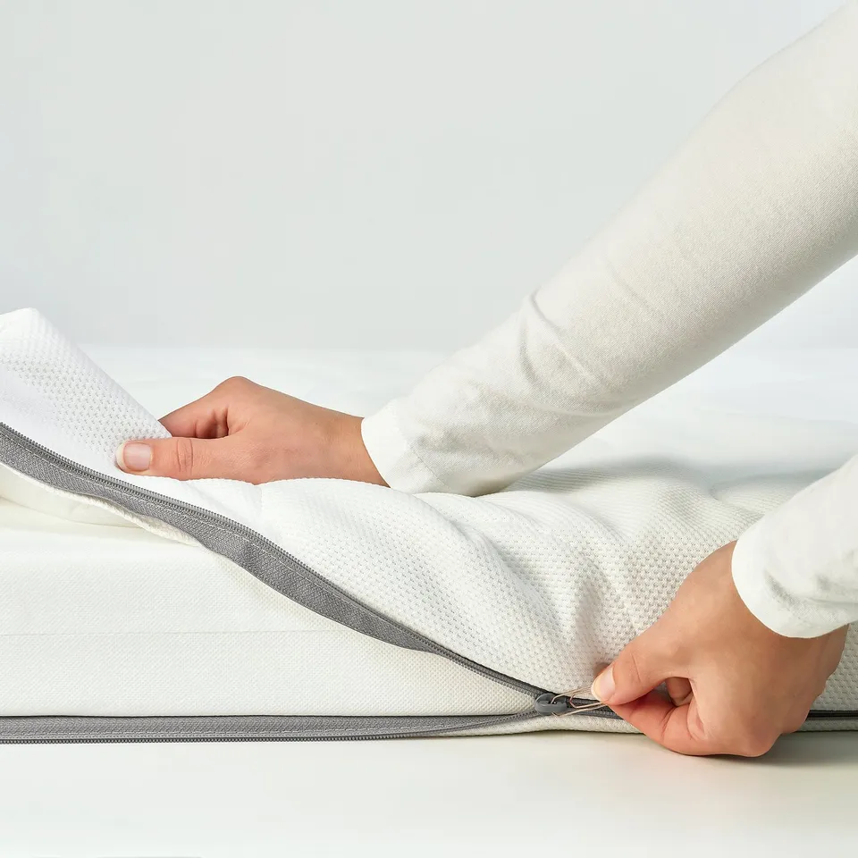 Person zips up white mattress, showcasing its easy-to-remove, machine washable cover for hygiene.