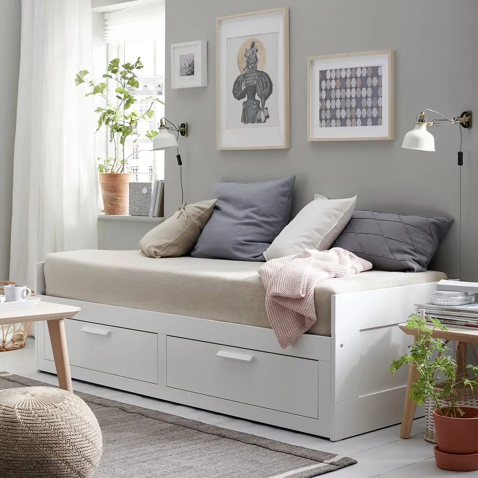 Modern minimalist living room with BRIMNES white daybed, grey pillows, wall art, plant, and side tables.