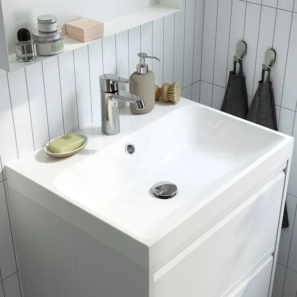 A modern bathroom sink with a chrome tap and soap dispenser. The tap has a cold-start feature to save water and energy. A black towel hangs nearby.