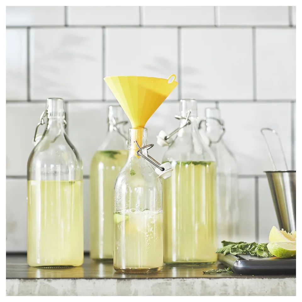 Bright yellow plastic funnel in clear glass bottle with homemade lemonade.