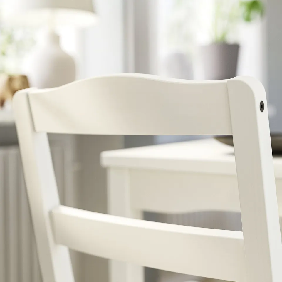 A close-up of a white wooden chair back and seat edge, part of the HAUGA dining set. It a simple, clean design.