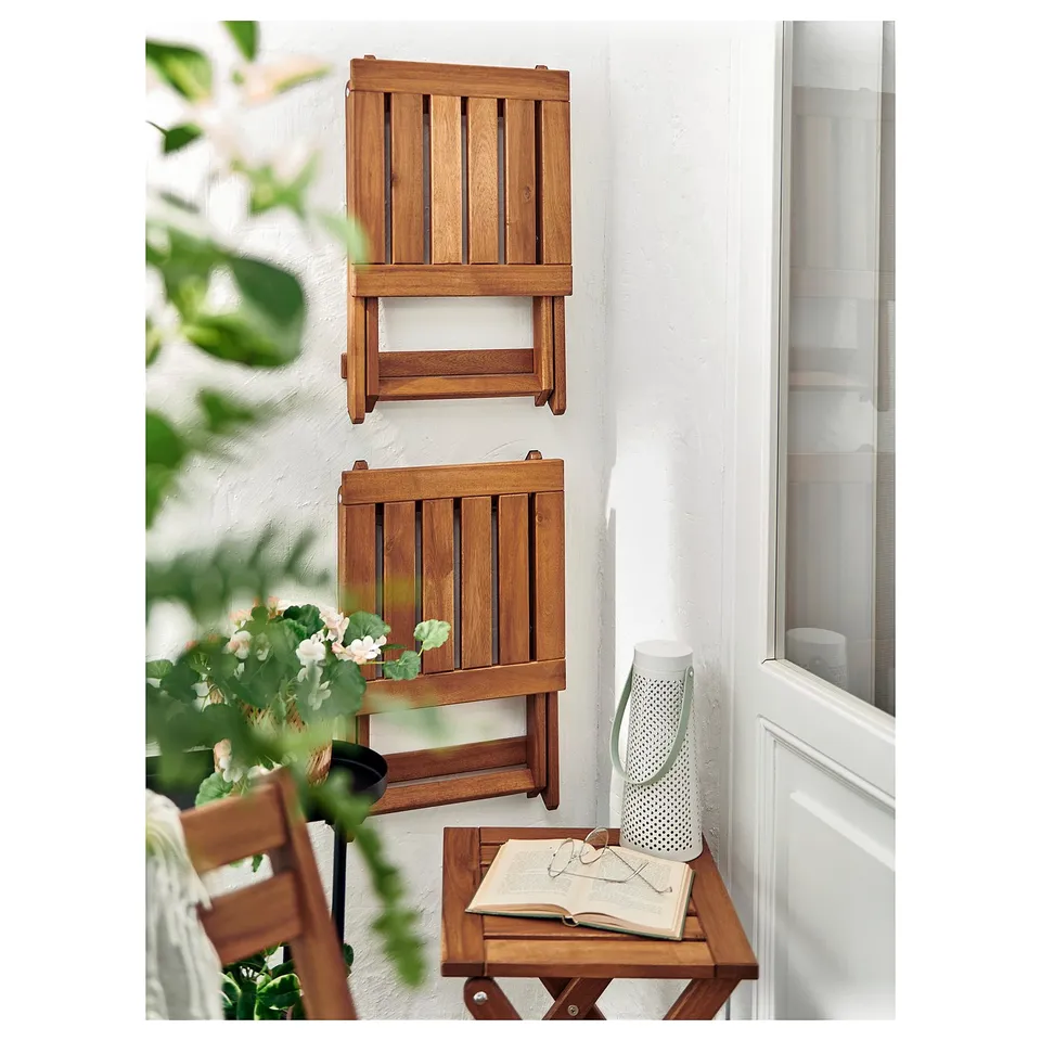 Two wooden folding chairs hang on wall above small table with book, vase, and glasses.