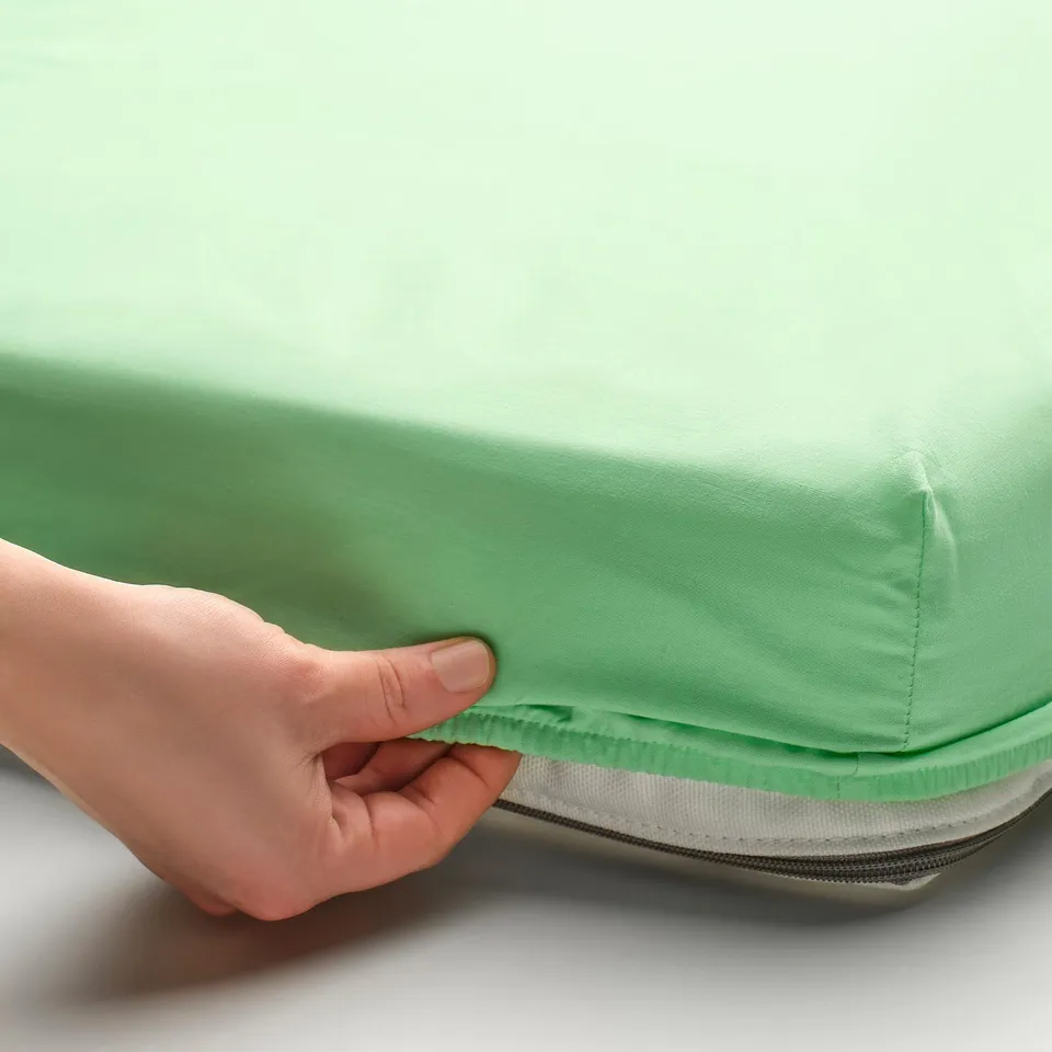 Hand holding green bed sheet with zip.