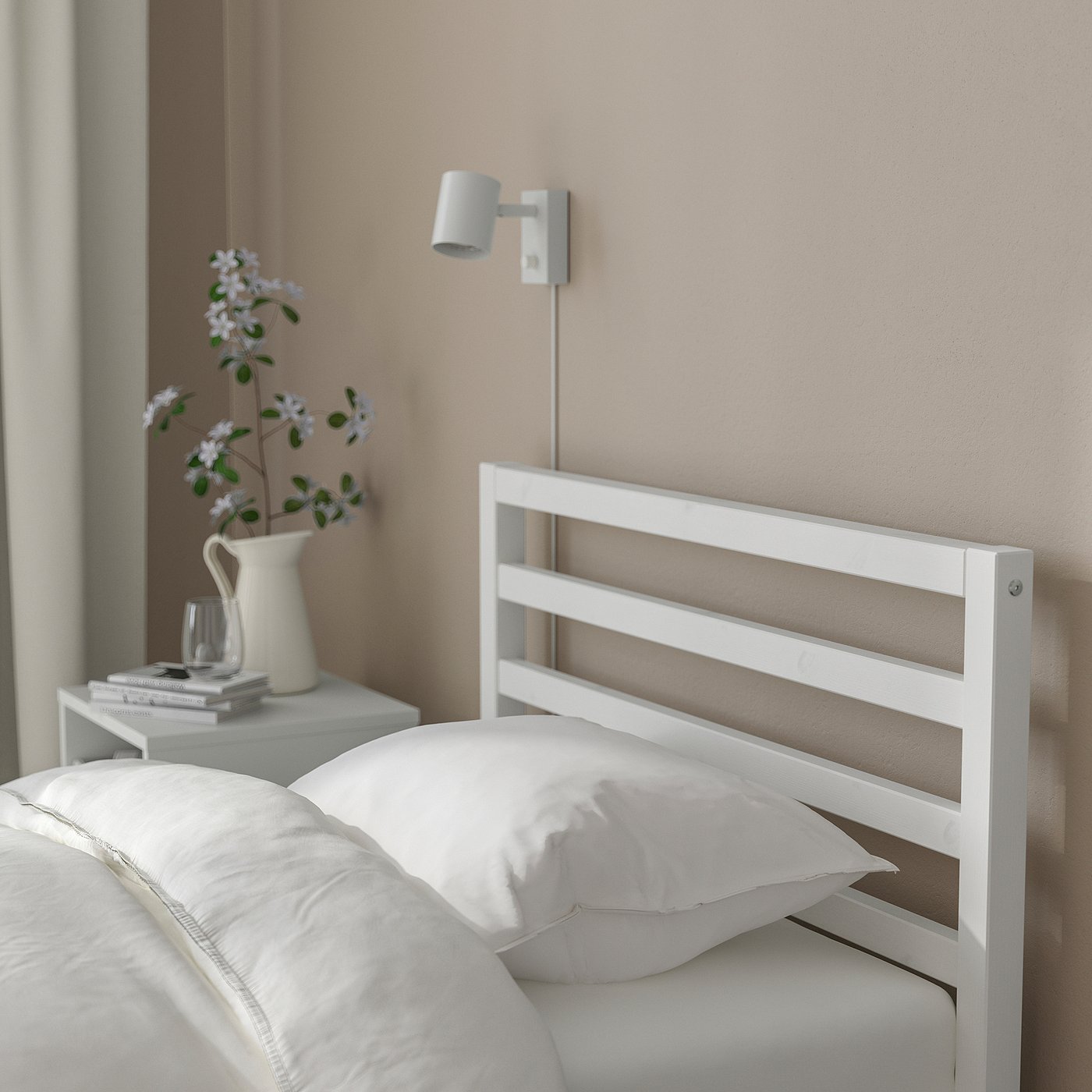 A simple, white wooden bed with a headboard, pillows, and a wall-mounted light for cosy reading.
