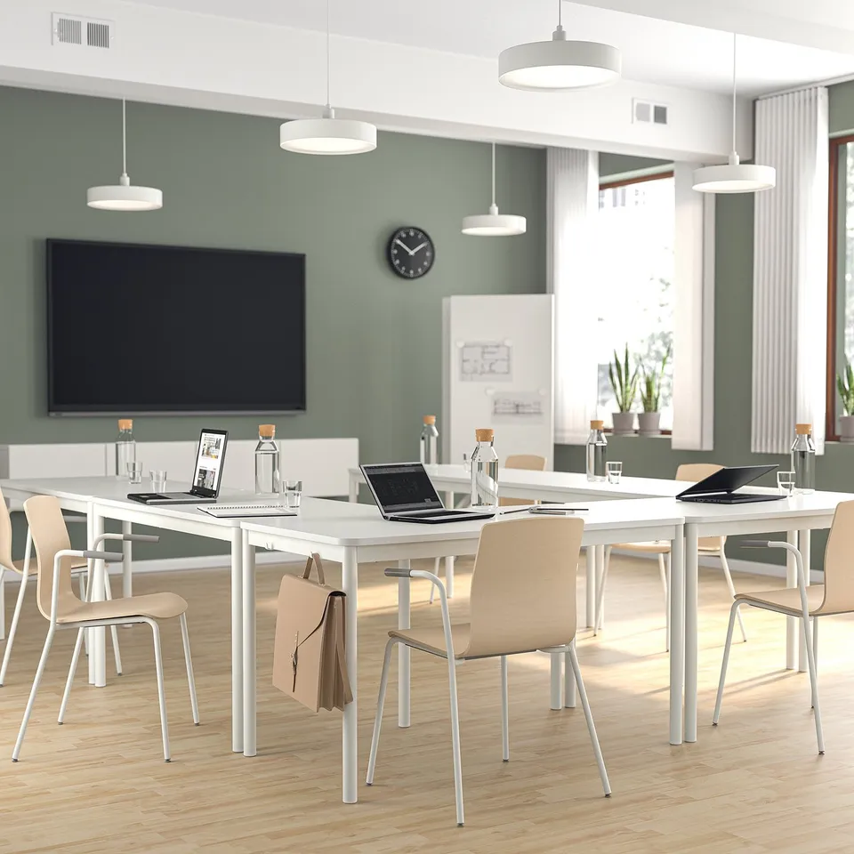 Modern conference room: white tables, laptops, beige chairs, green walls, large screen, bright.