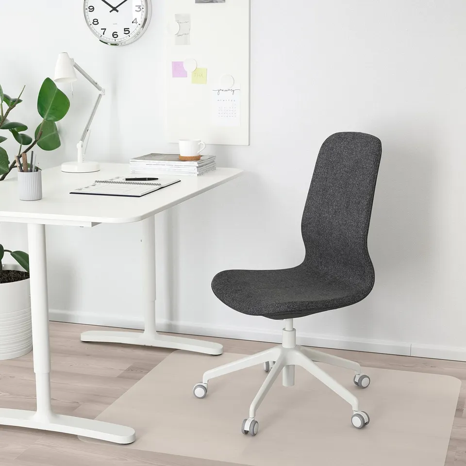 Minimalist home office with black LÅNGFJÄLL chair, desk, books, lamp, and clock.