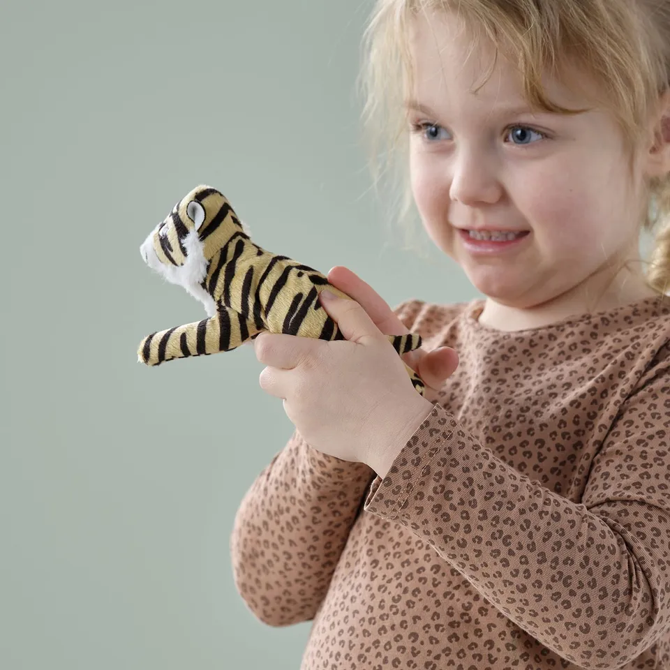A young girl holds a soft tiger toy, wearing a spotted shirt, enjoying the person plush companion.