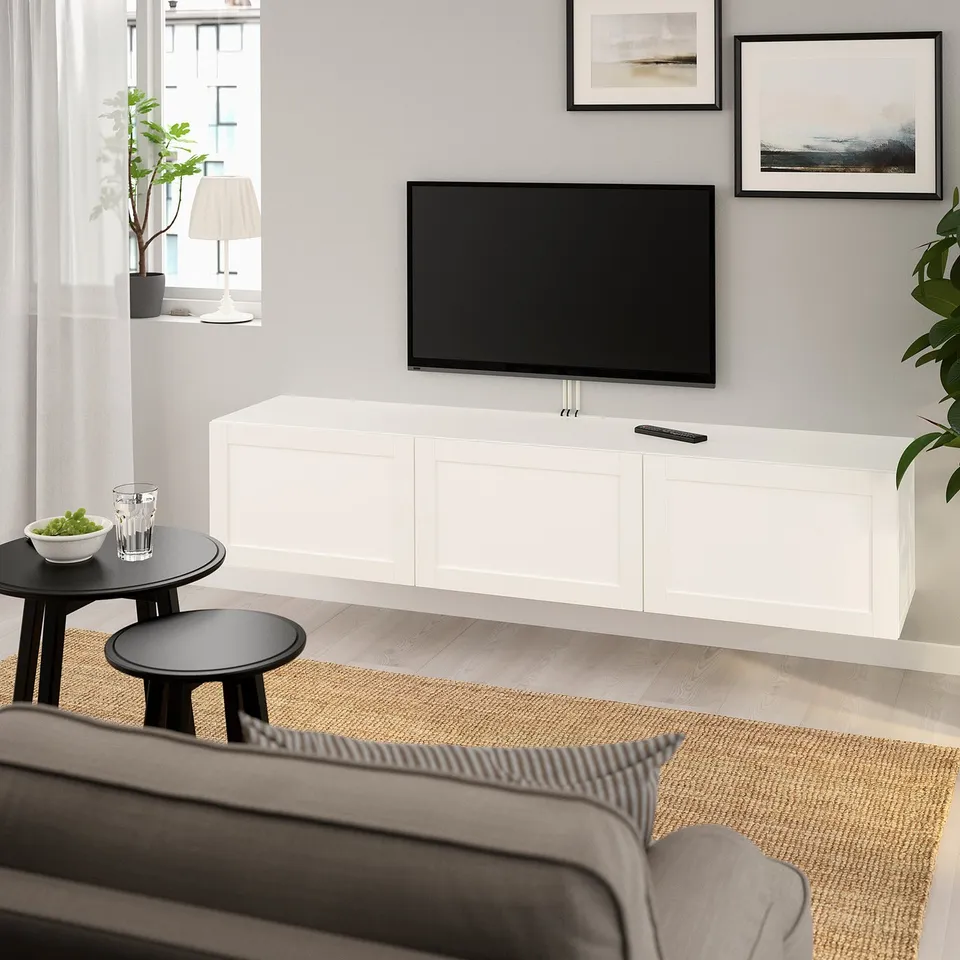 Modern living room with white BESTÅ tv bench, flat screen, grey sofa, fruit bowl, and art-themed wall.