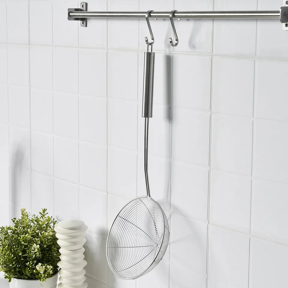 Stainless steel skimmer hangs on kitchen wall hook, ideal for draining liquids from pots.