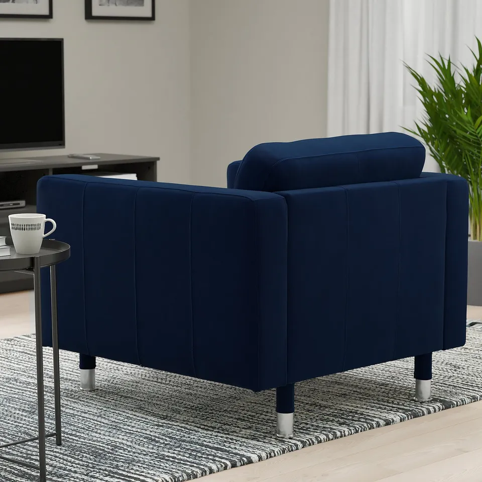A modern living room with a navy blue armchair, a small side table with a coffee mug, and a tv on a wooden stand. A plant and a rug are also present.