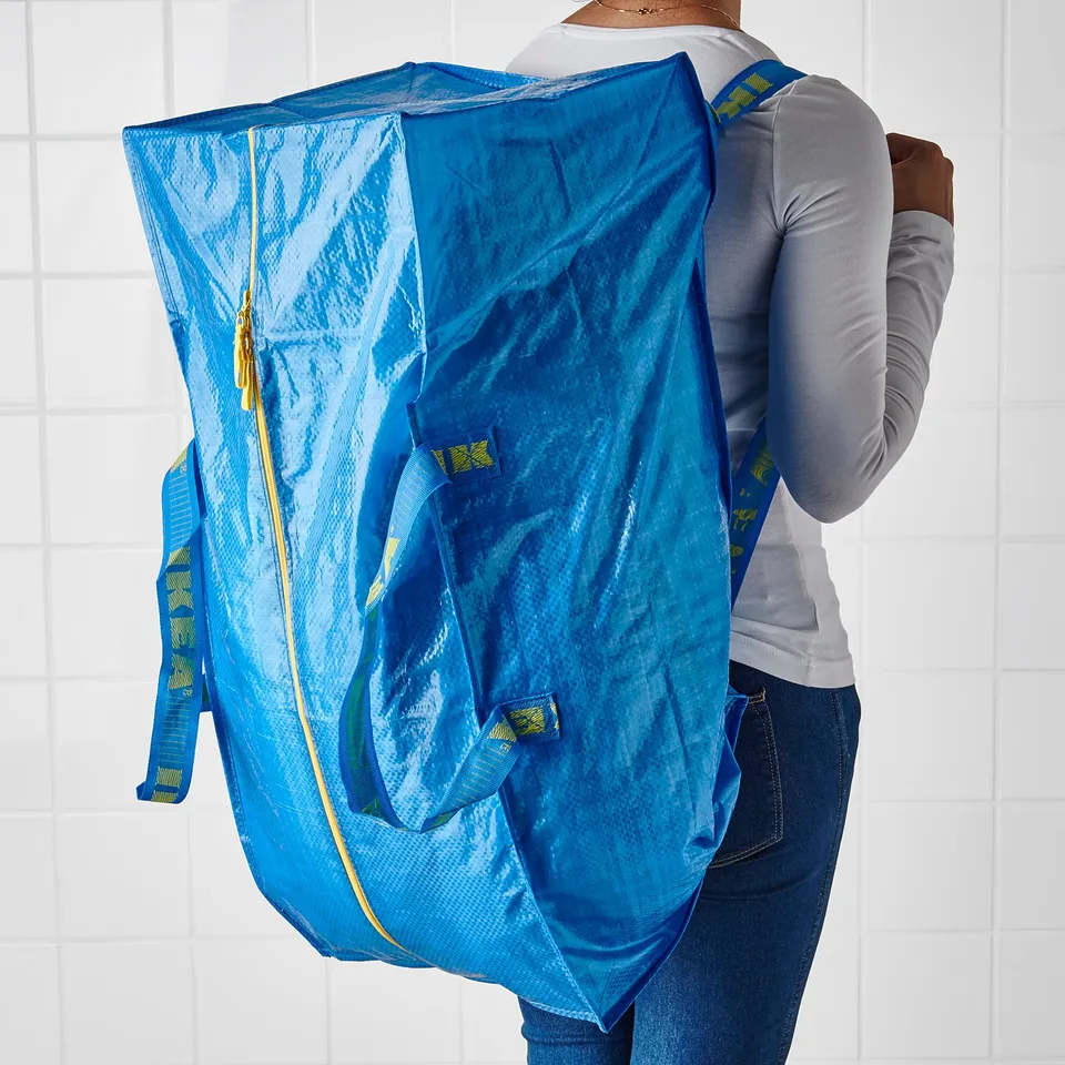 Person carries large blue FRAKTA shopping bag with yellow zip and straps over shoulder.