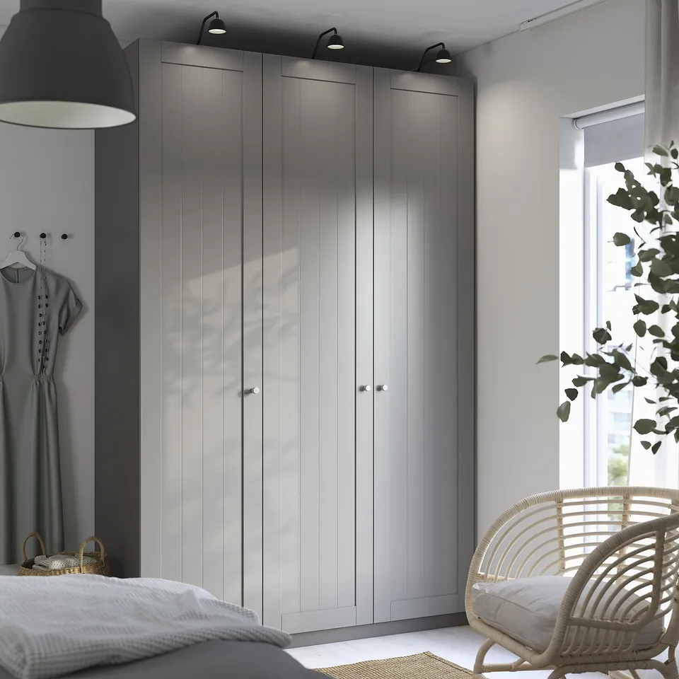 Modern bedroom with large PAX wardrobe in grey, three doors, integrated lighting, dark unit, large bed, chair, and plant.