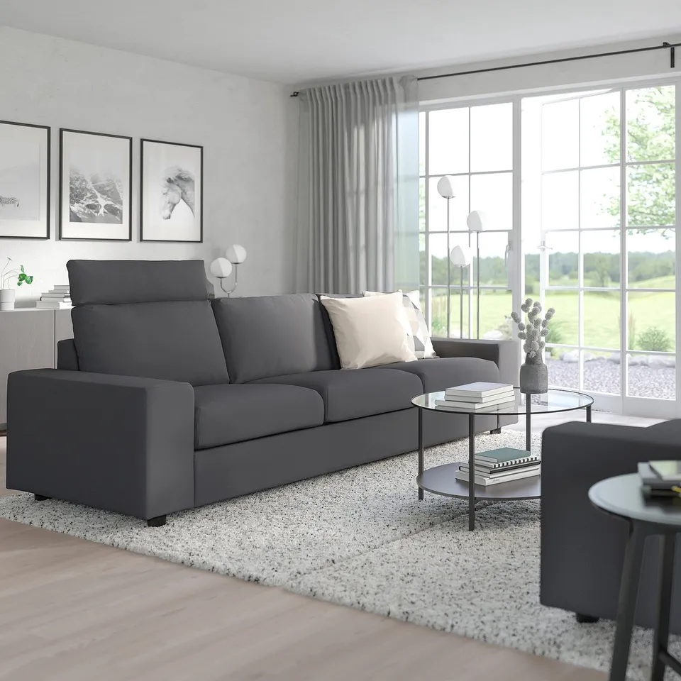 Modern living room with large grey VIMLE sofa, matching armchair, glass coffee table, and rug, set against white walls and large windows.