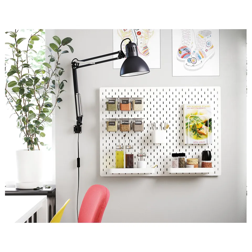 Organised workspace with adjustable black TERTIAL lamp, pegboard, plant, and colourful chair.