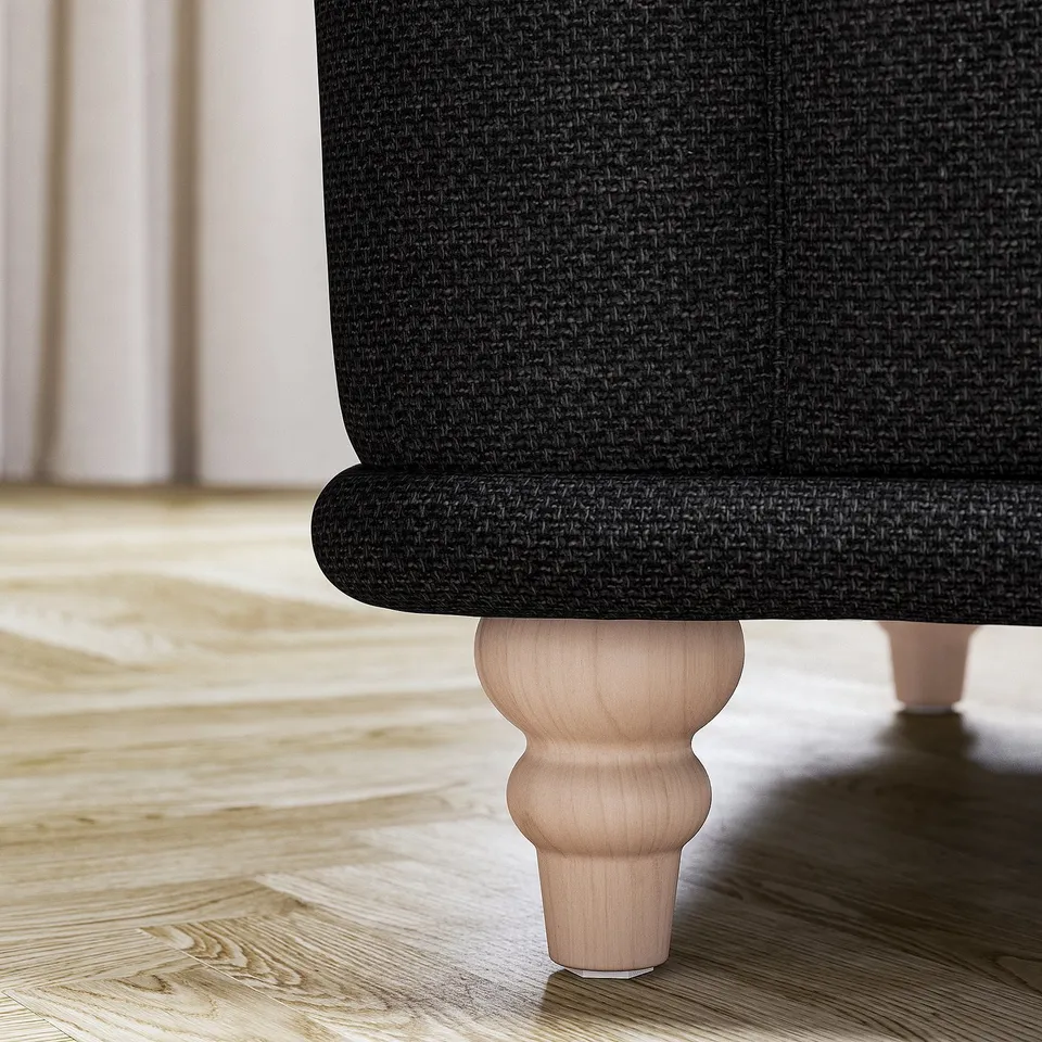 A corner of a dark grey VISKAFORS armchair with wooden legs on a wooden floor.