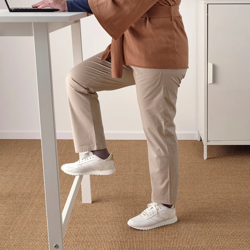 Person standing at high table with built-in footrest, using laptop. Ideal for quick, on-the-go work or meetings.